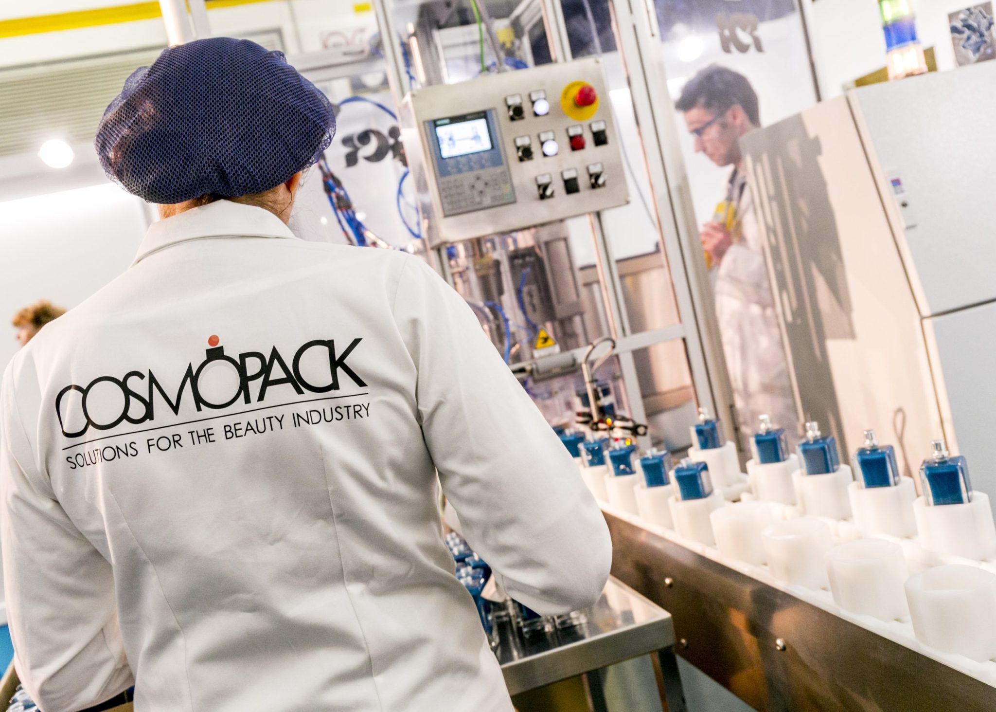 Personale con camice della manifestazione Cosmopack vincono a delle macchine di confezionamento esposte in fiera